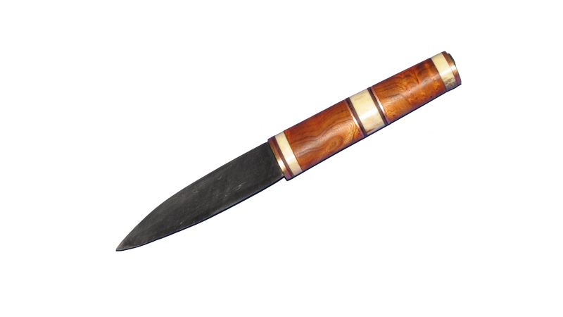 Dieses Messer hat eine Klinge aus Raffinierstahl in der ein Schneidenstahl eingelegt ist. Der Griff besteht aus Maserrüster mit Plättchen aus Messing, Kupfer, pflanzengegerbten Leder und Horn.